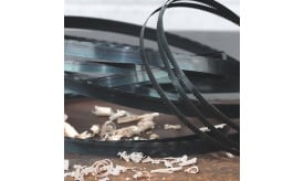 Metal bandsaw blades coiled on a surface with wood shavings scattered around, showcasing cutting tools and materials.